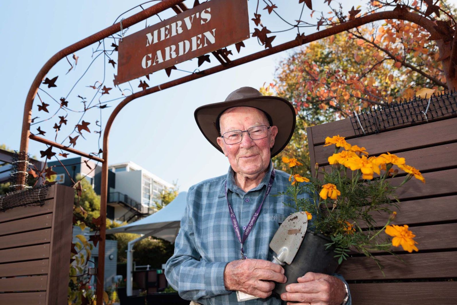 A volunteer is smiling at the camera, with a pot of flowers in his hands.