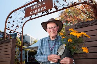 A volunteer is smiling at the camera, with a pot of flowers in his hands.