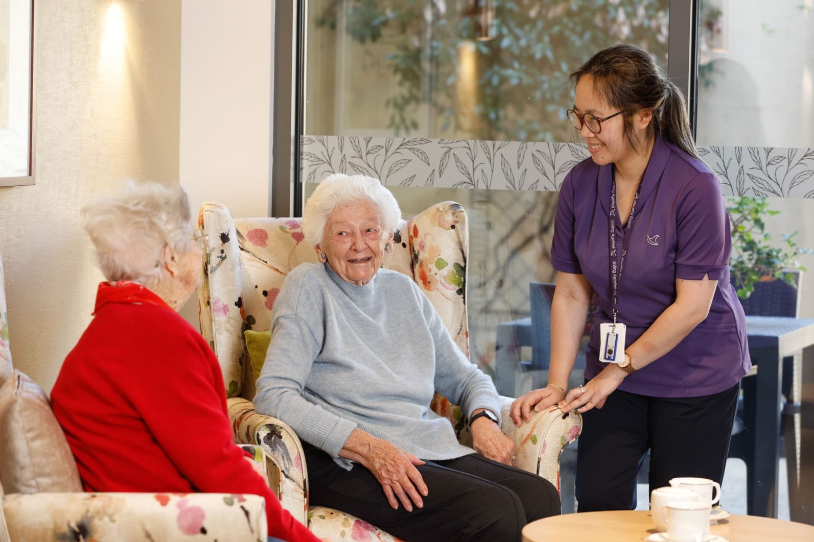A staff member chats with two residents in the lounge area