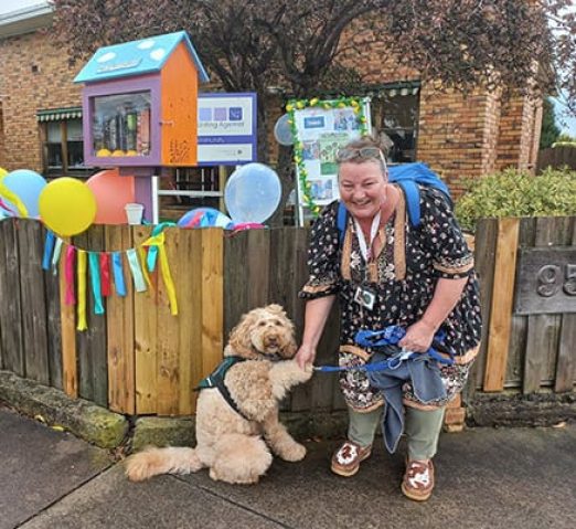 A woman shakes her dog's paw in front of the Street Library, which is decorated in ribbons and balloons.