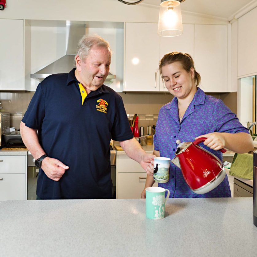 A Home Care Worker is pictured using a kettle in a customer's kitchen. The customer is also in sight.